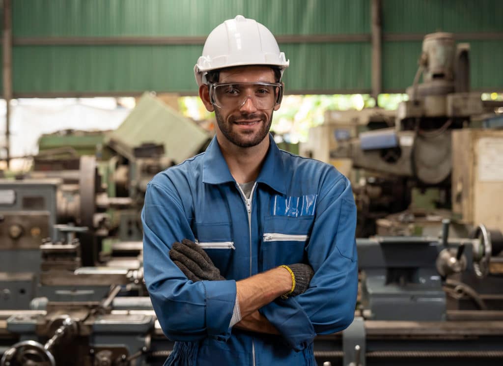 Male factory worker working and standing in front of manufacturing machinery